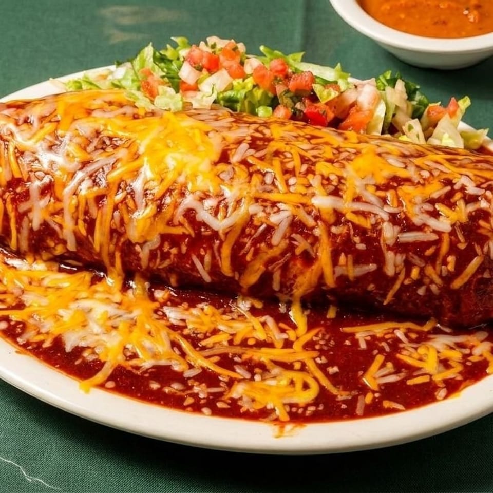 Smothered burrito covered in melted cheese and red sauce, with a side salad and two small bowls of salsa.