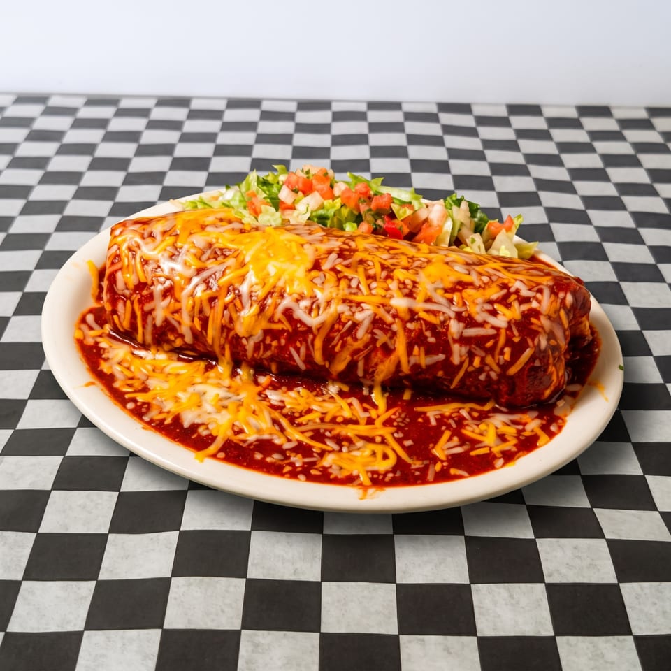 A large, smothered burrito covered in red sauce and melted cheese, with a side of lettuce and pico de gallo.